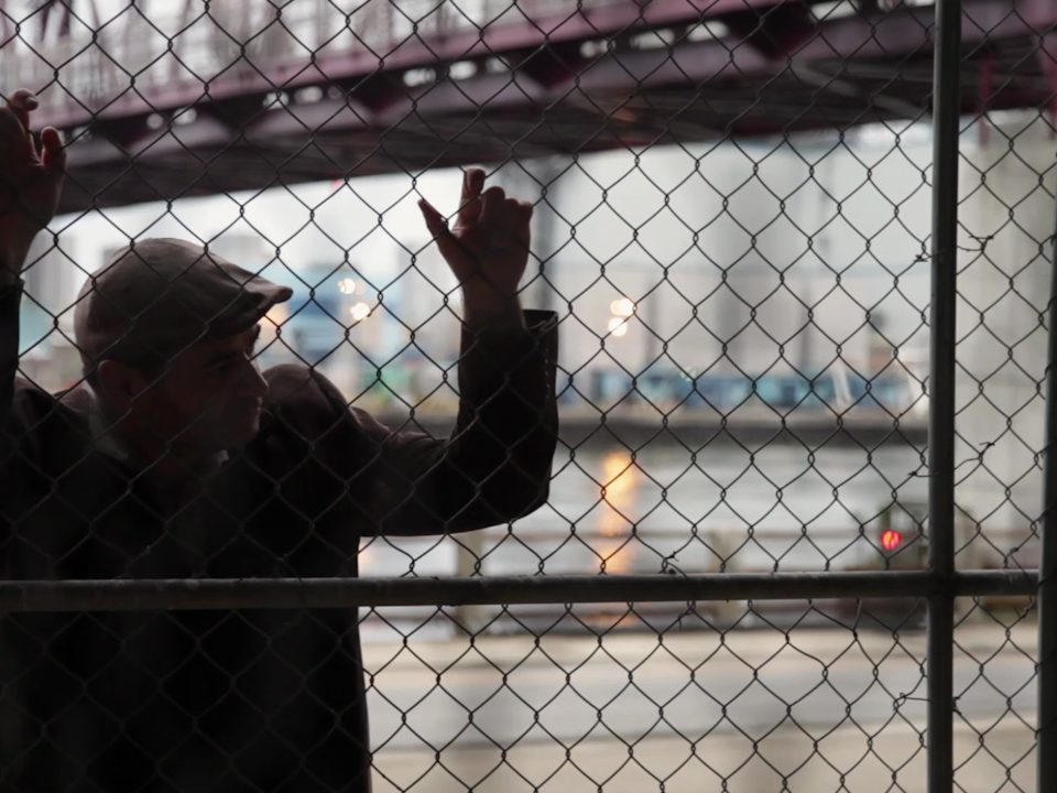 Frame from the Marco Luccio documentary — the artist at a fence, Postcards scene